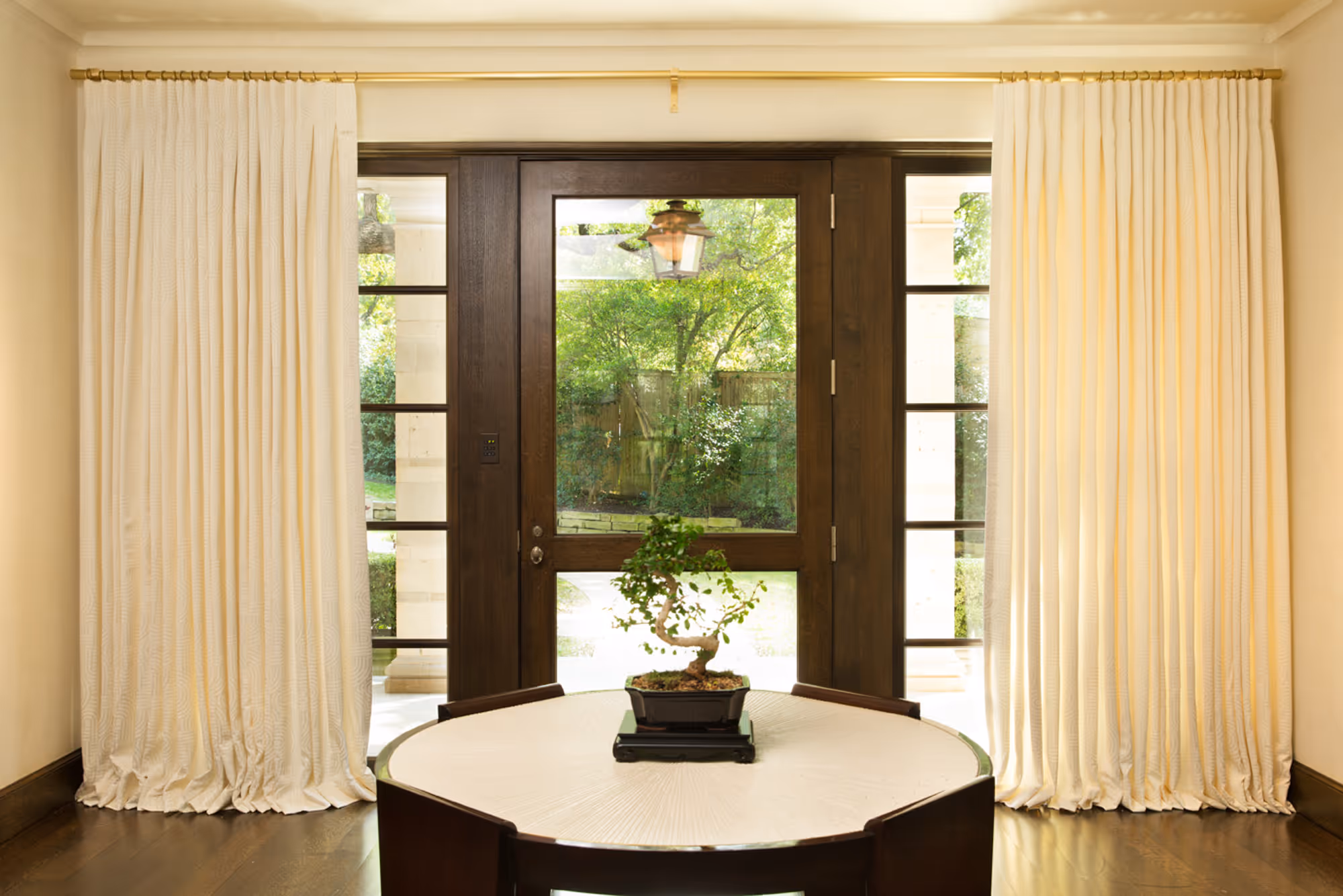 Elegant drapery framing a glass door entrance in a modern living room in Dallas, TX, featuring a bonsai tree centerpiece.
