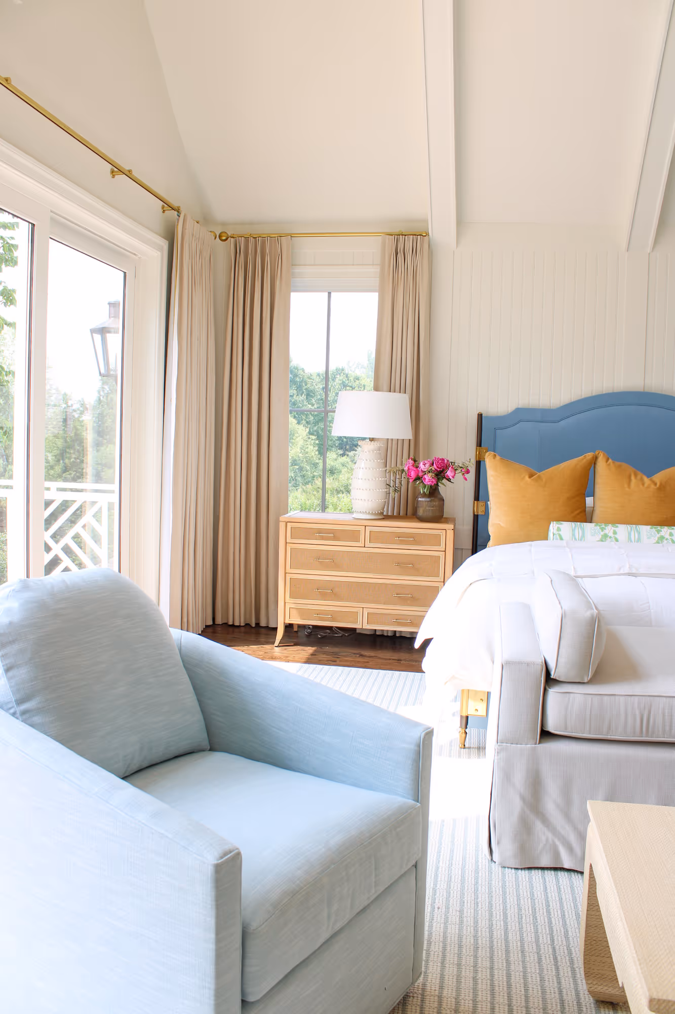 Light and airy bedroom with a blue upholstered headboard, beige drapes, and a light blue accent chair in arlington, va.
