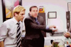 Two men in an office, with one man animatedly moving his arms as if dancing or gesturing.