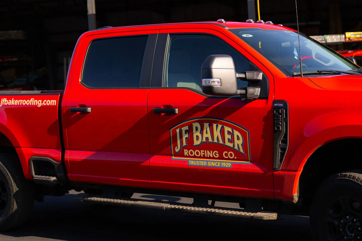 Red pickup truck with JF Baker Roofing Co. logo and website jfbakerroofing.com on the side.