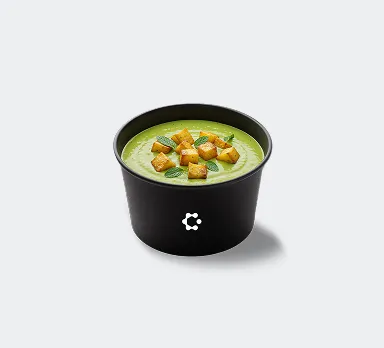 A black bowl with green soup topped with croutons and herbs, featuring a white Circus icon on the front.