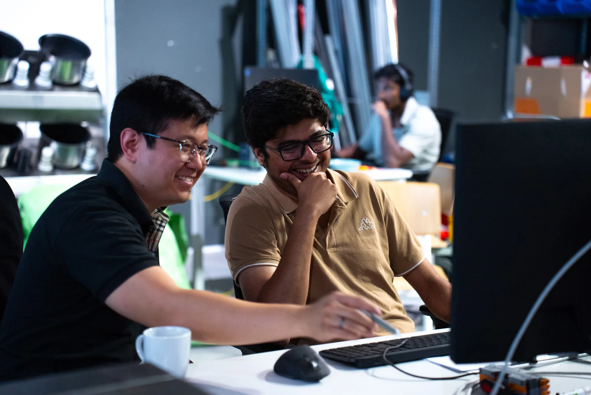Two engineers smiling and working together at a computer in an office or lab setting.