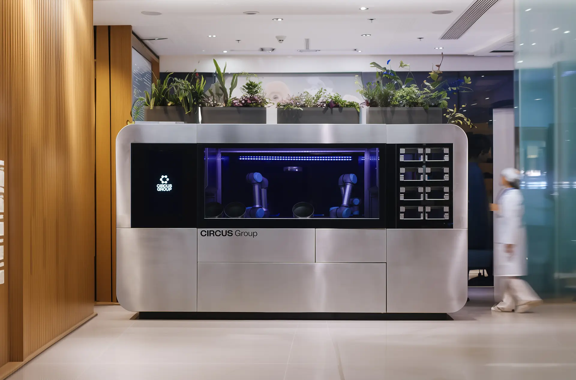 CA-1 Series 4 robotic kitchen by CIRCUS Group installed in a hospital setting, featuring dual robotic arms, a sleek stainless steel design, and decorative plants on top.
