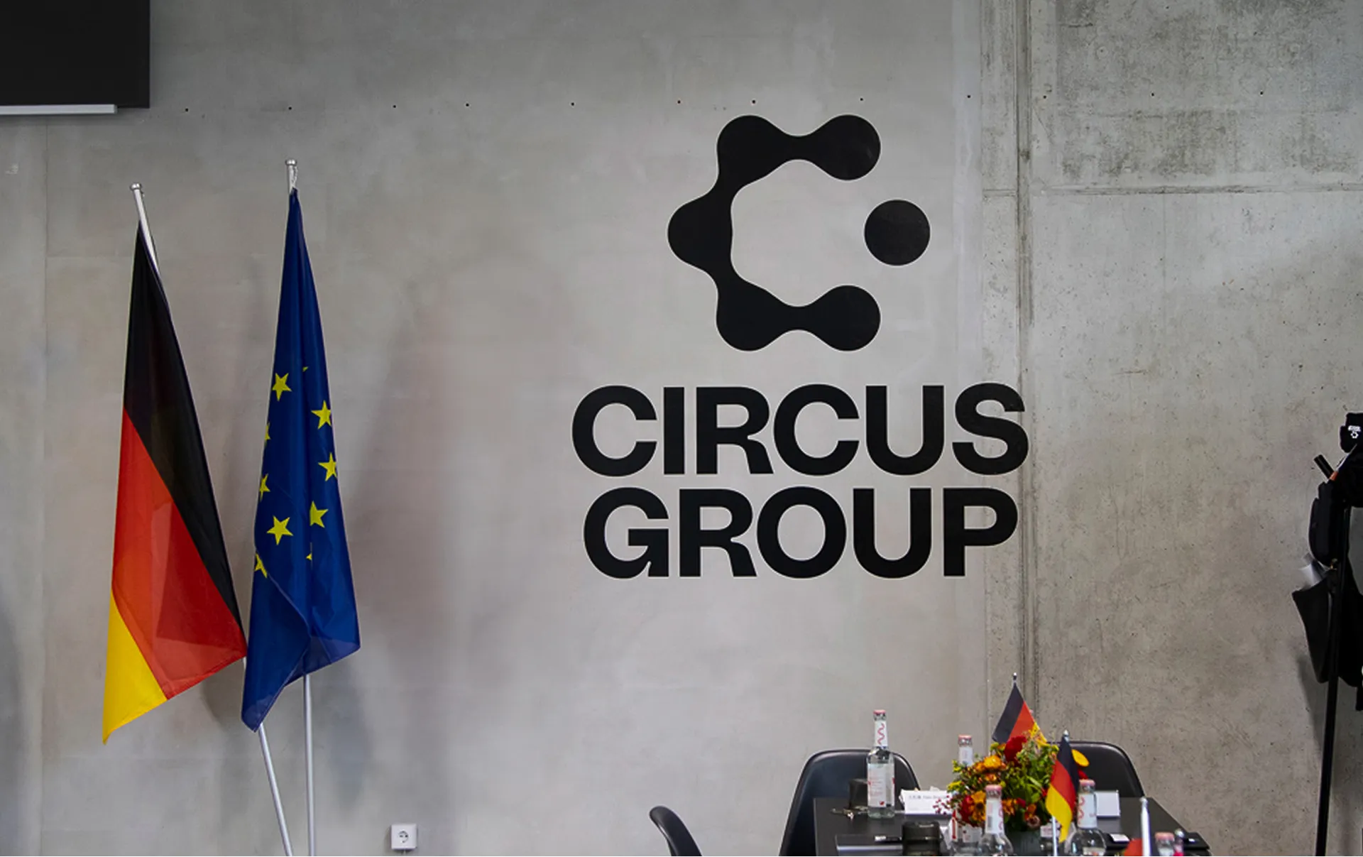 Circus Group meeting room with German and EU flags beside a concrete wall displaying the company logo, and a conference table set for a formal discussion.