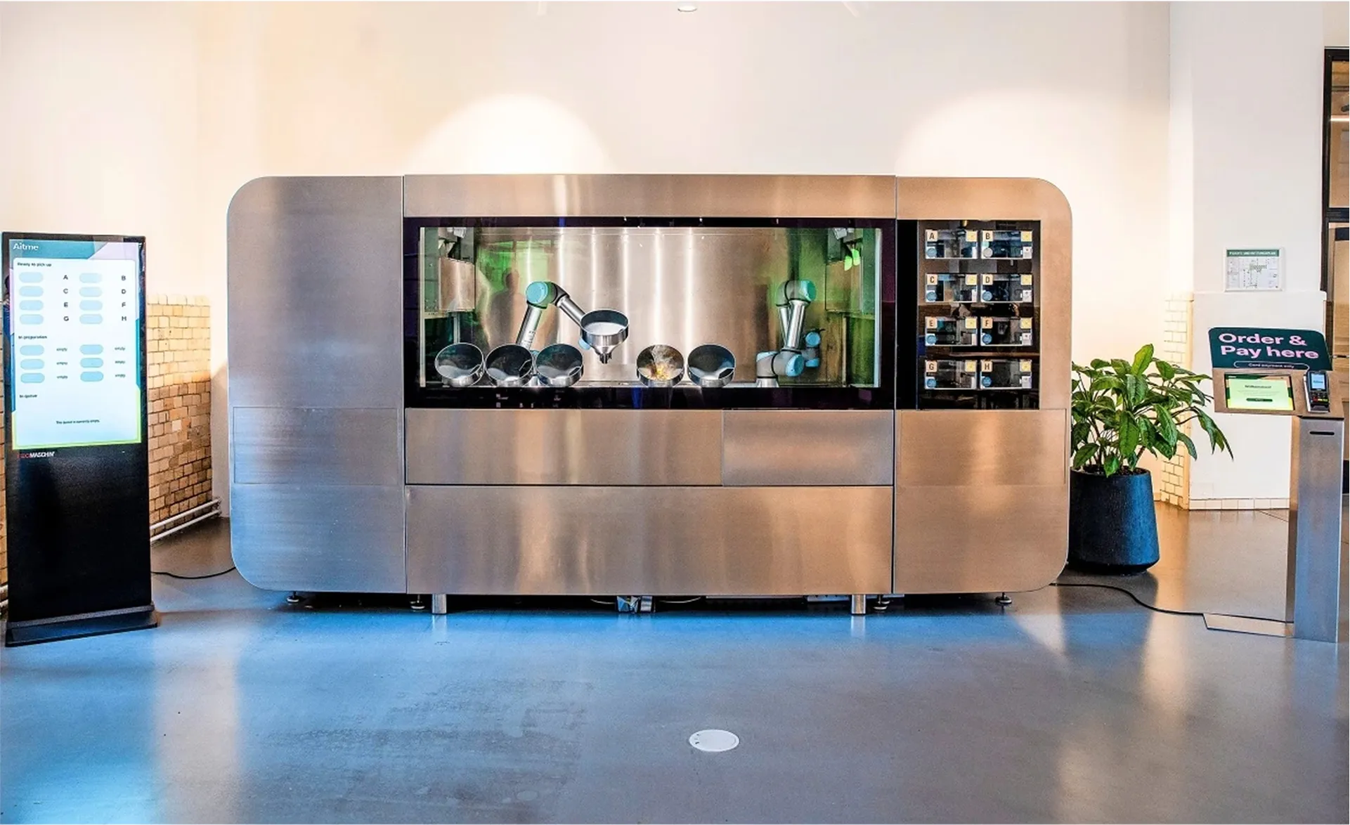 First CA-1 prototype deployed in a field setting, fully assembled and active with robotic arms inside and a user interface kiosk on the left for order placement.