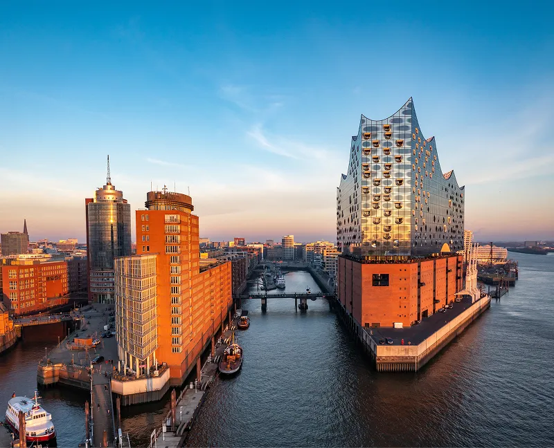 Aerial view of Hamburg's HafenCity with the iconic Elbphilharmonie concert hall at sunset, reflecting in the Elbe River.