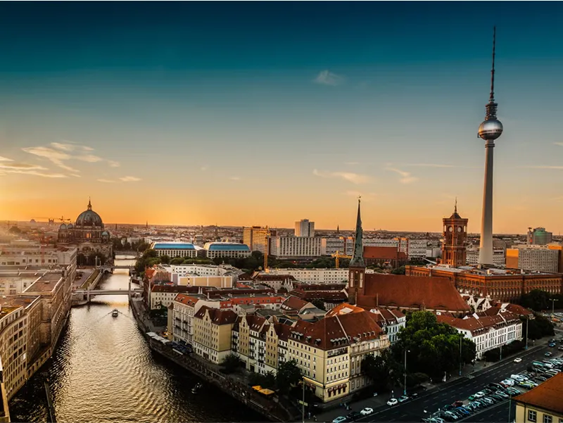 Panoramic view of Berlin at sunset featuring the Fernsehturm (TV Tower), Berlin Cathedral, and Spree River with historic and modern architecture.