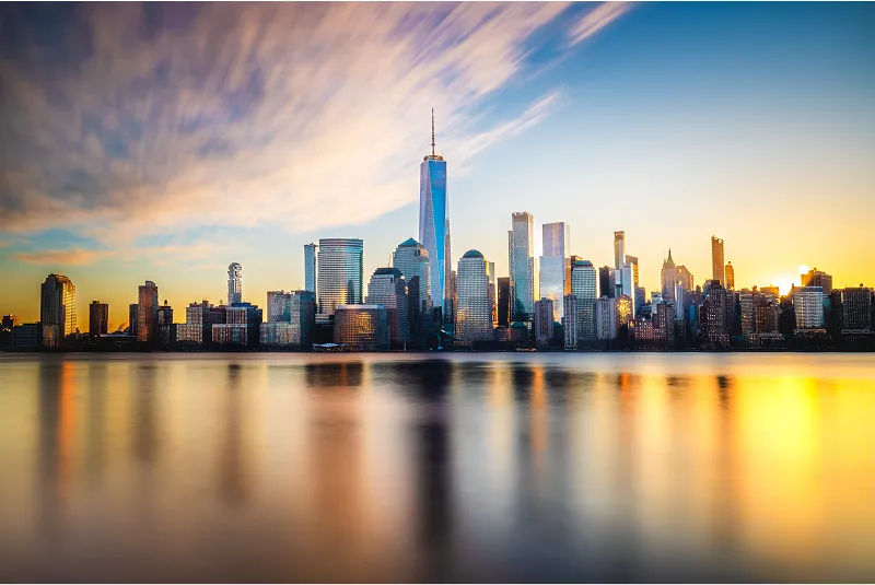 Sunset view of the New York City skyline featuring One World Trade Center reflecting on the Hudson River.