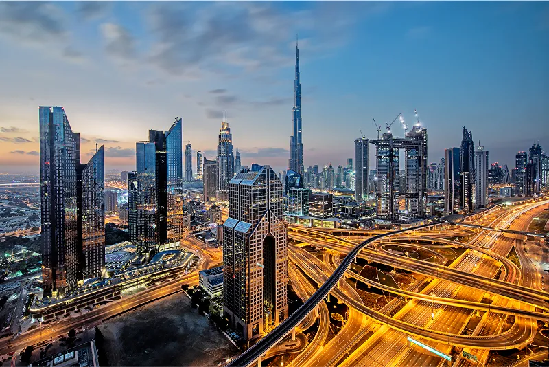 Evening skyline of Dubai featuring the Burj Khalifa and illuminated highways weaving through futuristic skyscrapers under a dramatic sky.