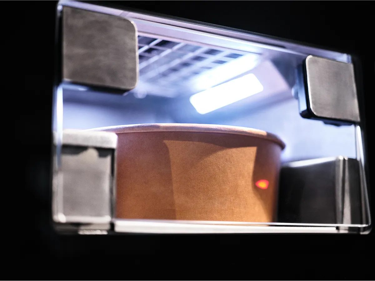 Close-up of a CA Series food container placed inside an illuminated automated delivery compartment of the CIRCUS robotic kitchen system.