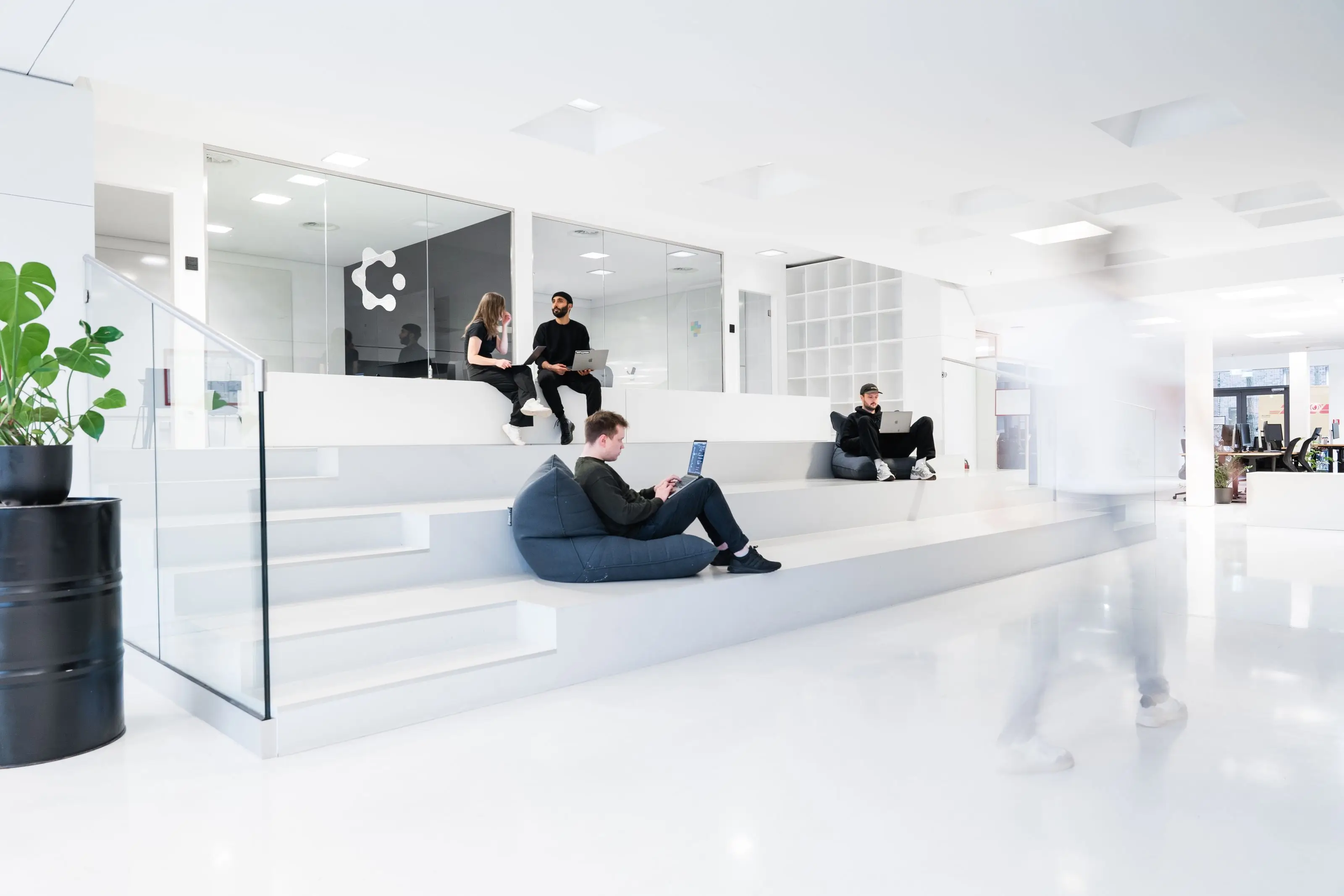 Modern bright office space with tiered seating where people work on laptops and have a conversation.