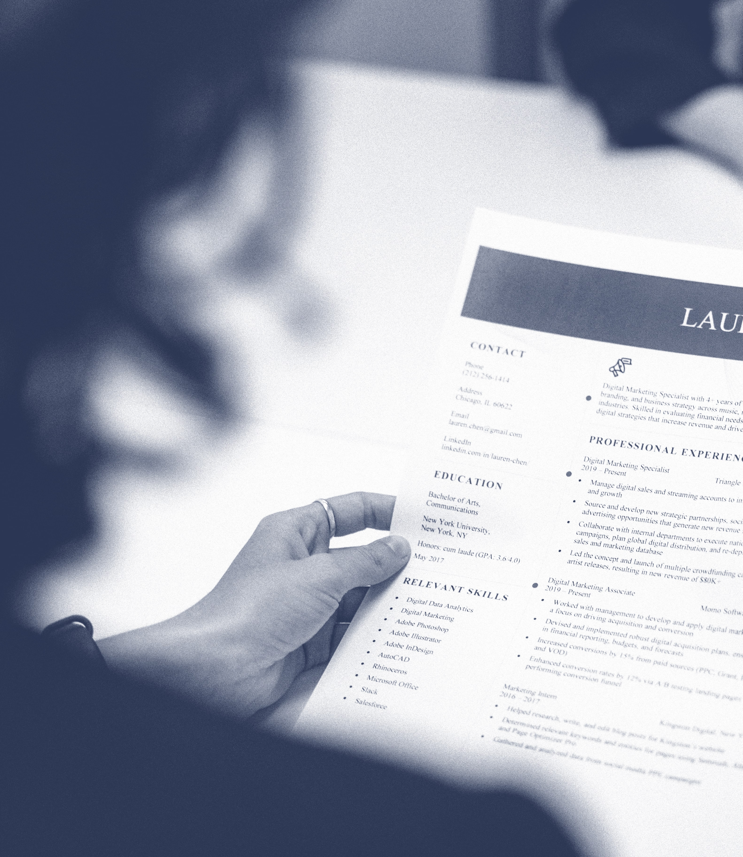 Person holding and reading a printed resume with sections including contact, education, relevant skills, and professional experience.