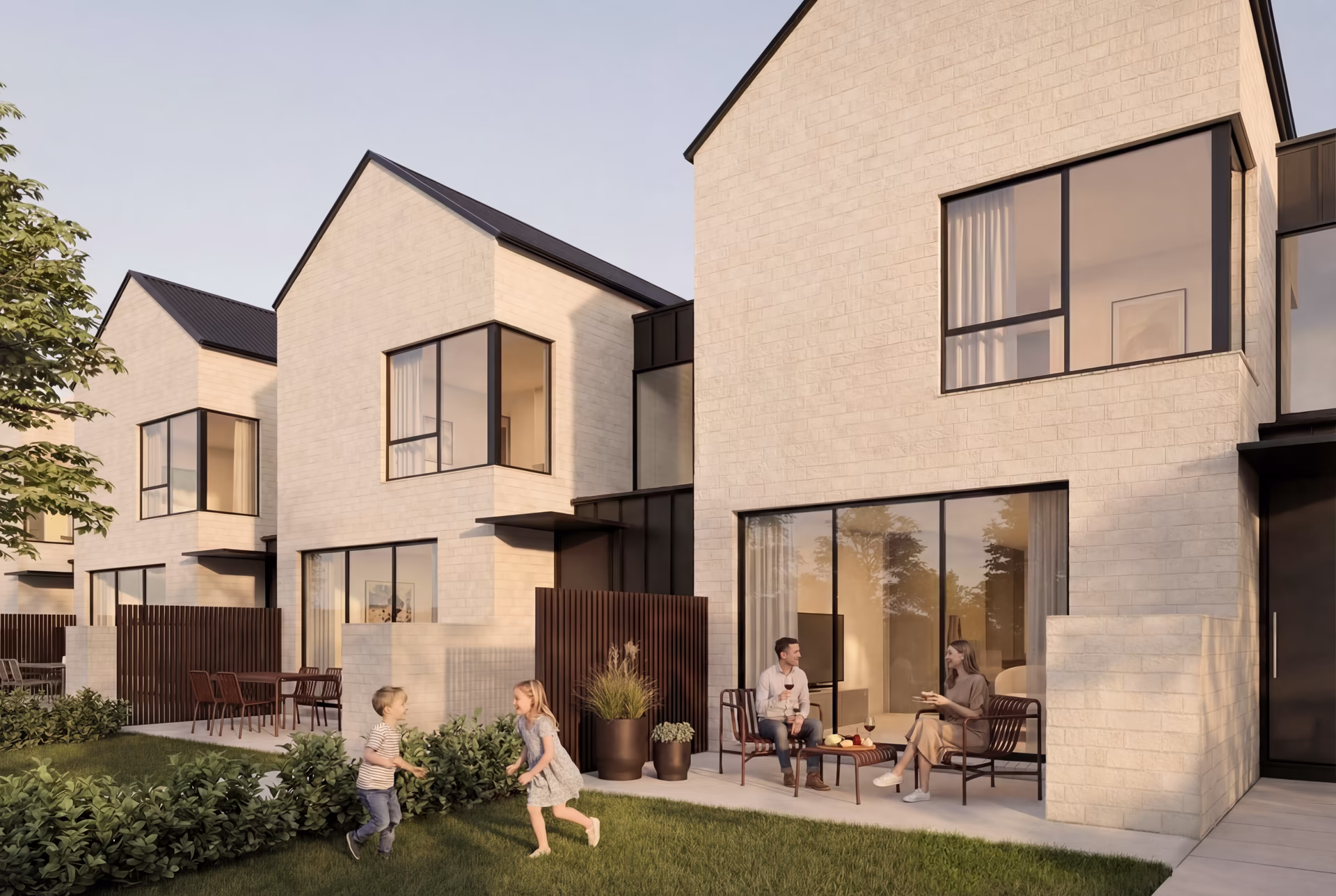 Modern beige brick townhouses with large windows and a patio where a man and a woman sit, and two children play on the grass.