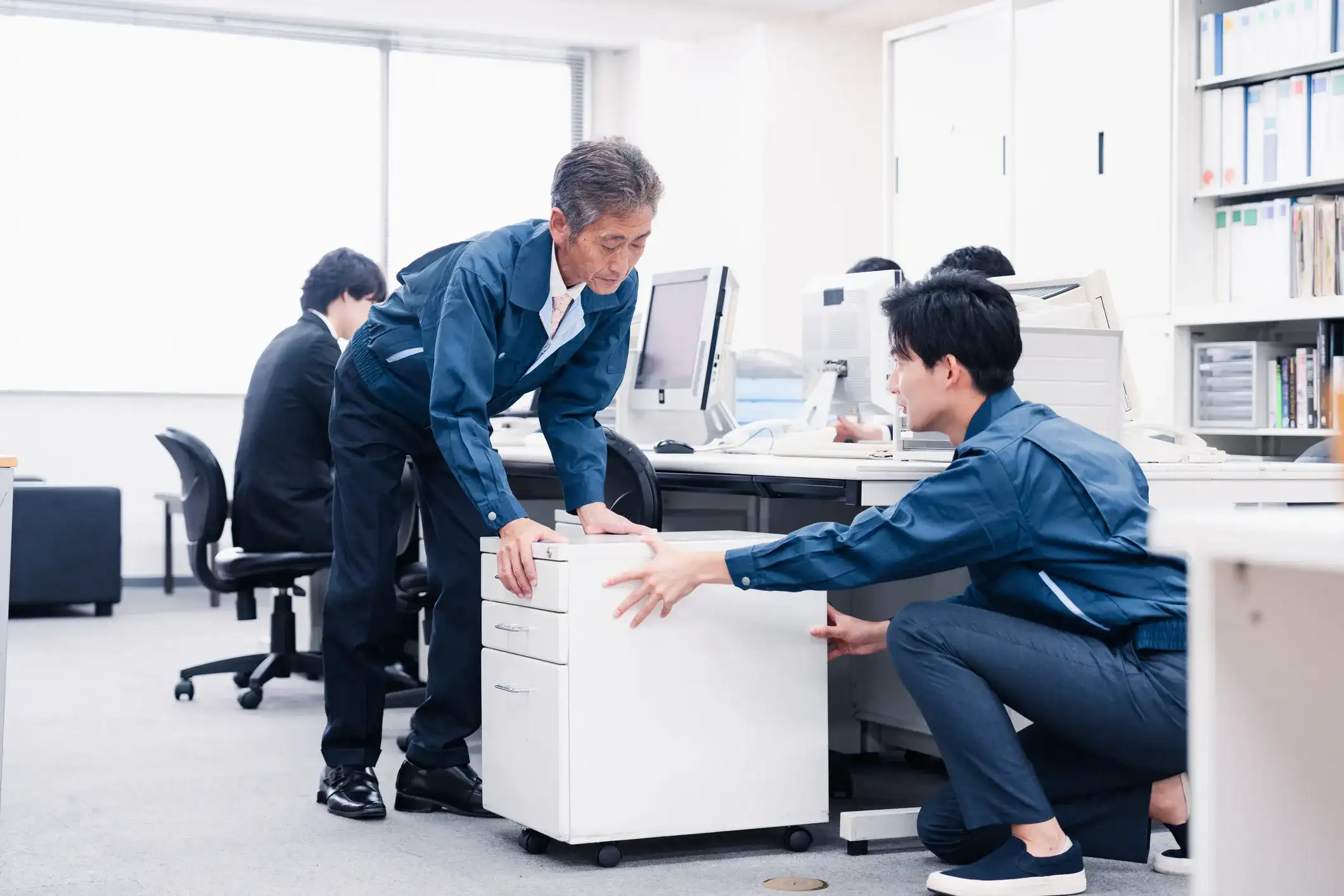 Office movers repositioning a filing cabinet during a business relocation