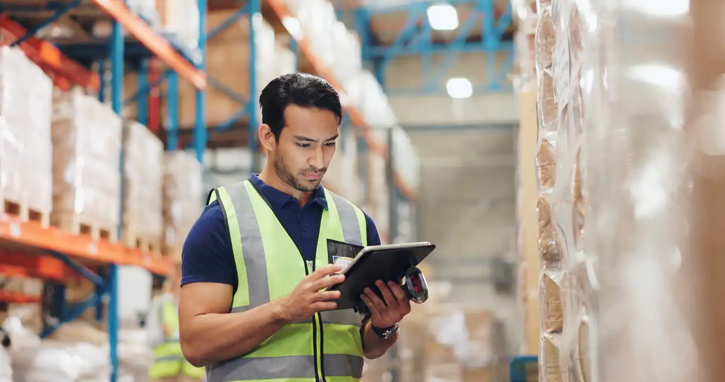 A warehouse worker in a high-visibility vest using a tablet to scan inventory.