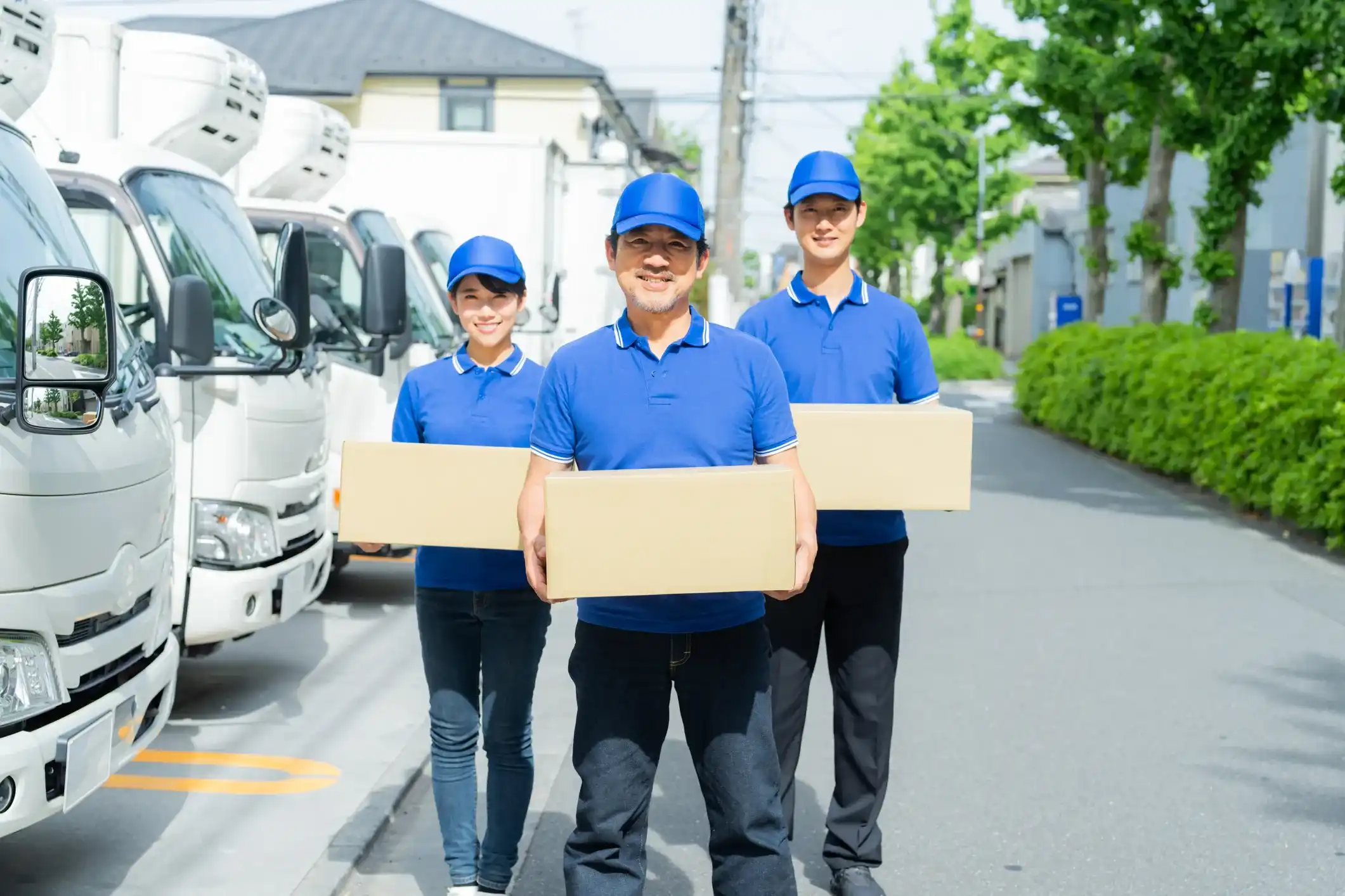 Professional moving team holding boxes in front of parked delivery trucks