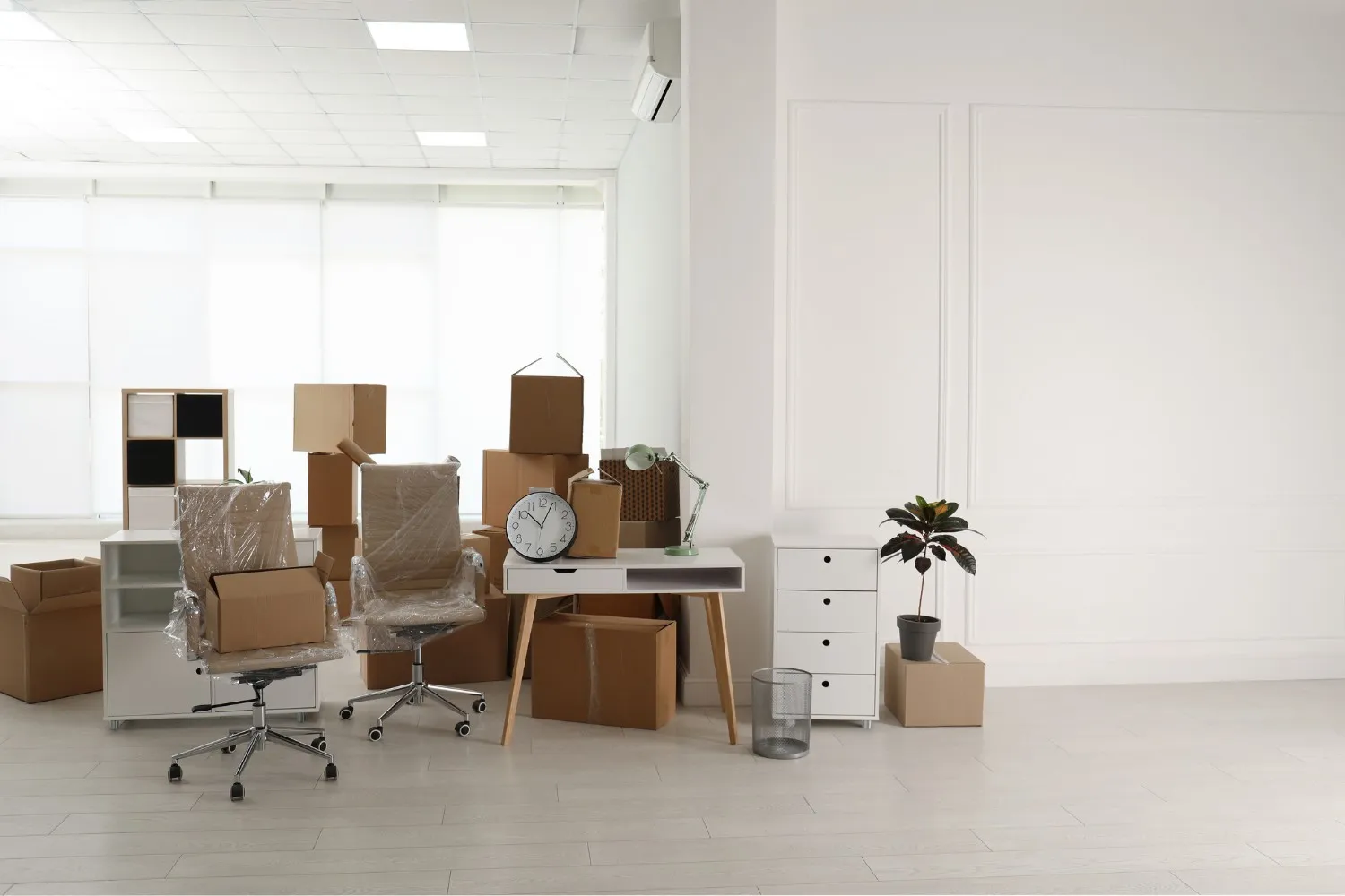 Open cardboard box with binders and rolled-up document in a modern office with wrapped chair and desk.