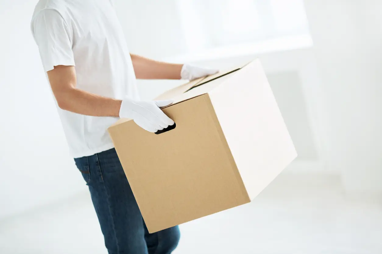 Side view of a person wearing white gloves and a white t-shirt carrying a cardboard box