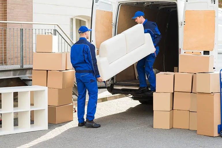 Movers unloading white sofa from truck.