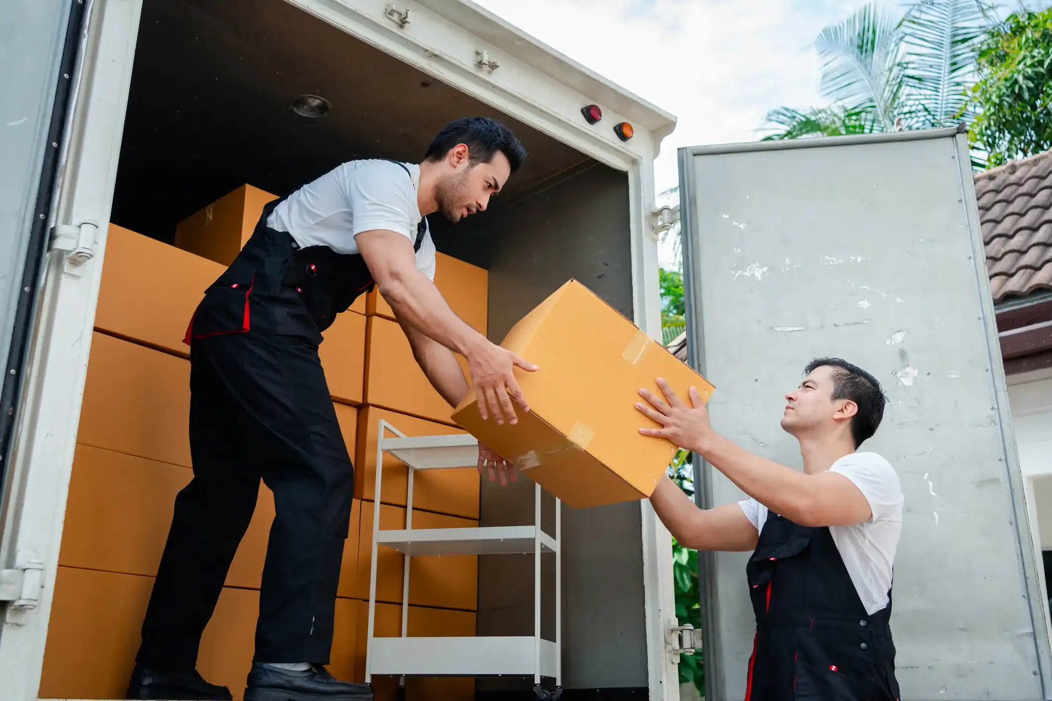 Movers handing a packed cardboard box from a truck during home moving