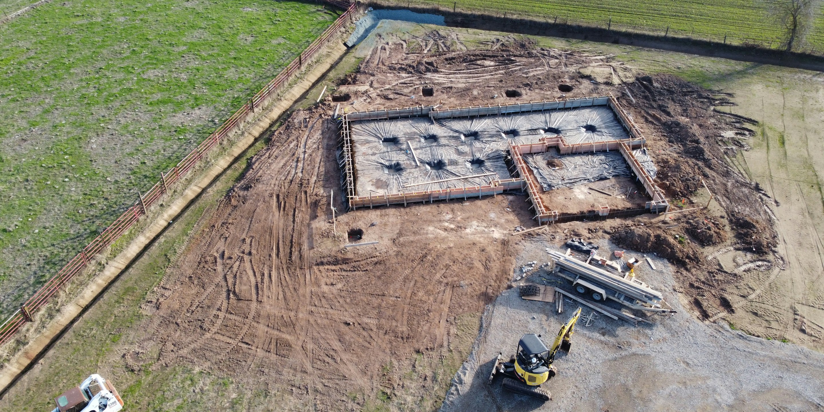 Luftaufnahme einer Baustelle mit Erdarbeiten, Fundament und Bagger