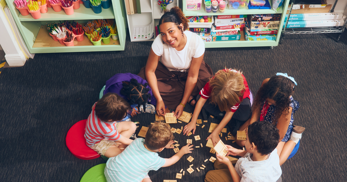 A teacher sitting in a circle with students who are working in their assignments. 
