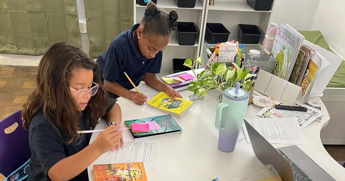 The student writing on a paper within a classroom. 