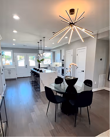 Modern kitchen with white cabinetry, a large island with barstools, and a dining area featuring a glass table and black chairs under a modern starburst chandelier.