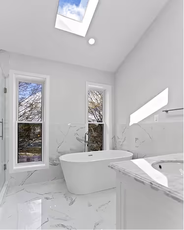 Bright modern bathroom with a freestanding bathtub, marble floor, large windows, and skylight.