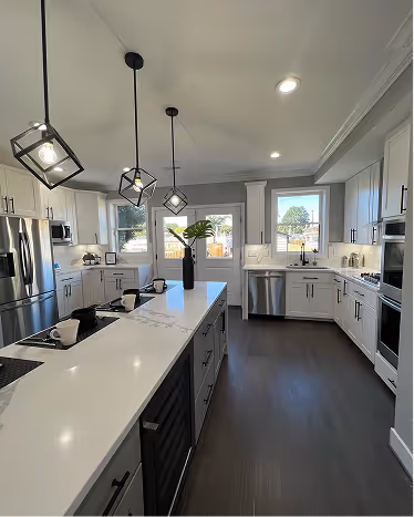 Modern kitchen with white cabinetry, a large central island with a vase of flowers, pendant lights, stainless steel appliances, and large windows.