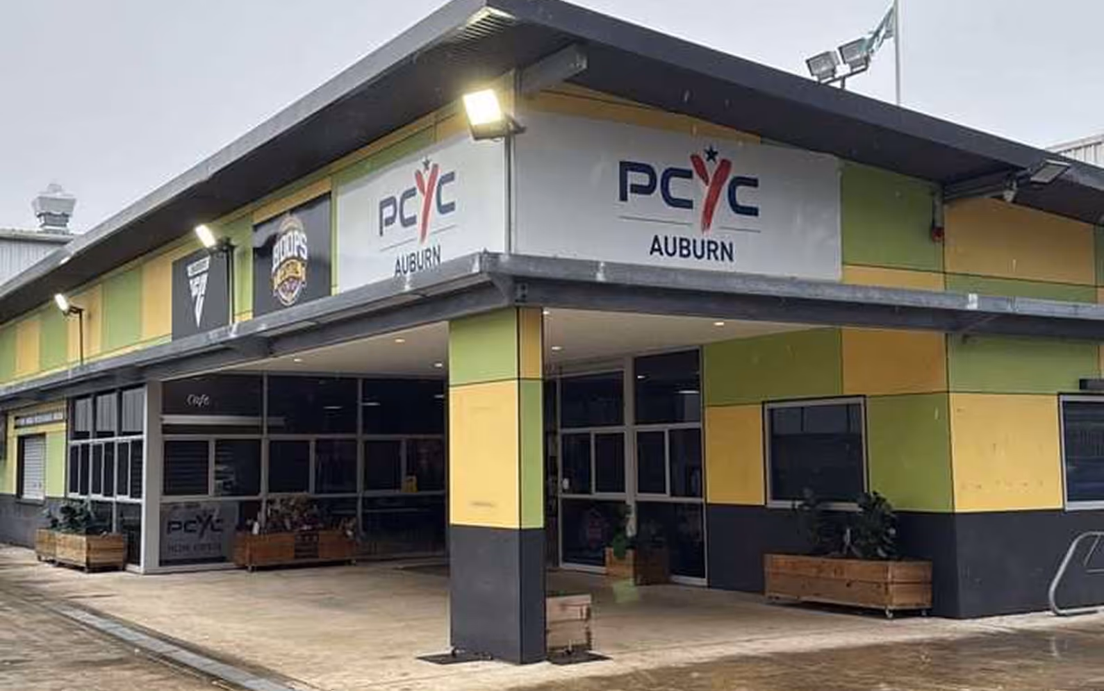 Exterior view of the PCYC Auburn building with its logo on signs above the entrance and windows, featuring a green, yellow, and black color scheme.