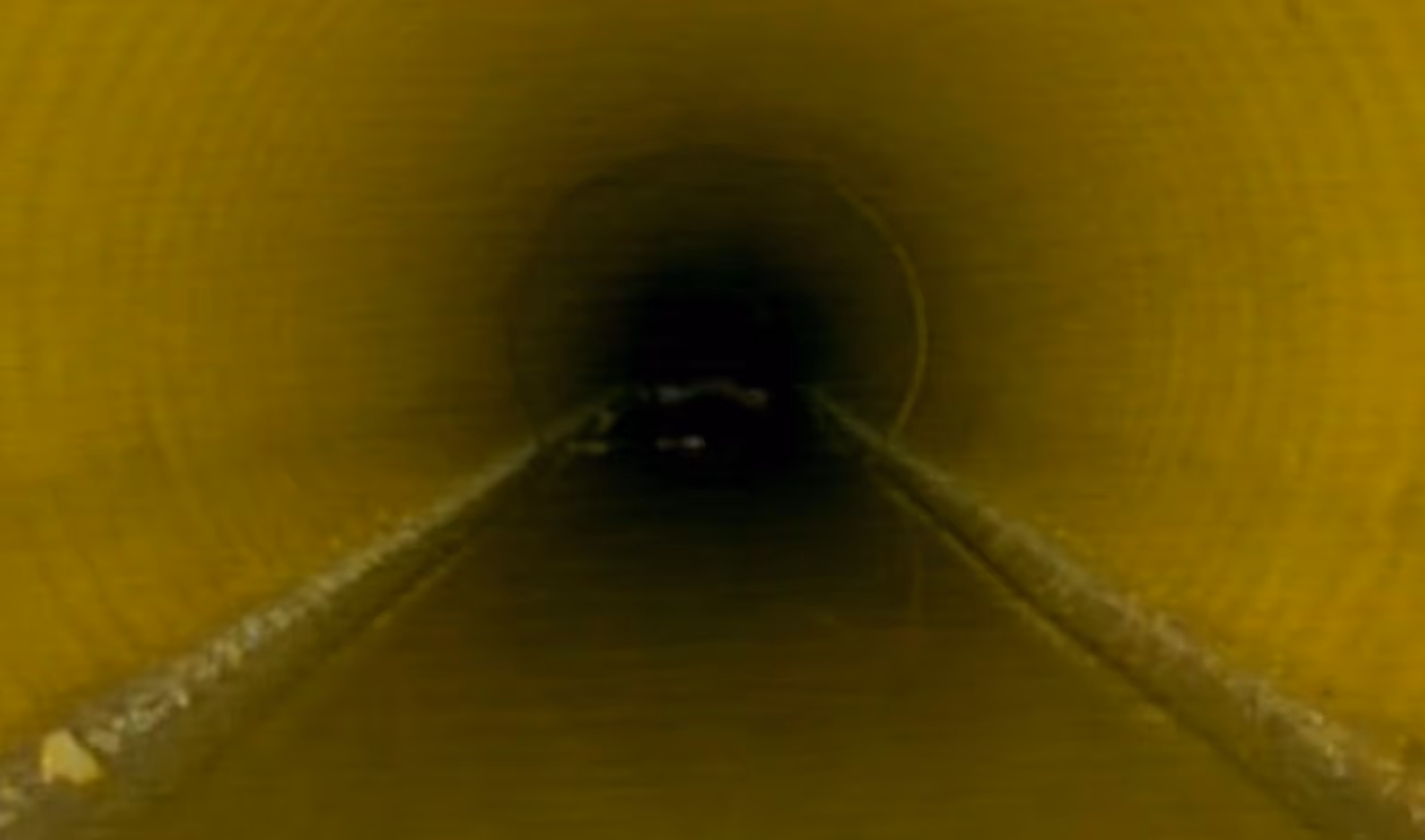 View looking through a long yellow tunnel with dark interior and partially visible floor edges.