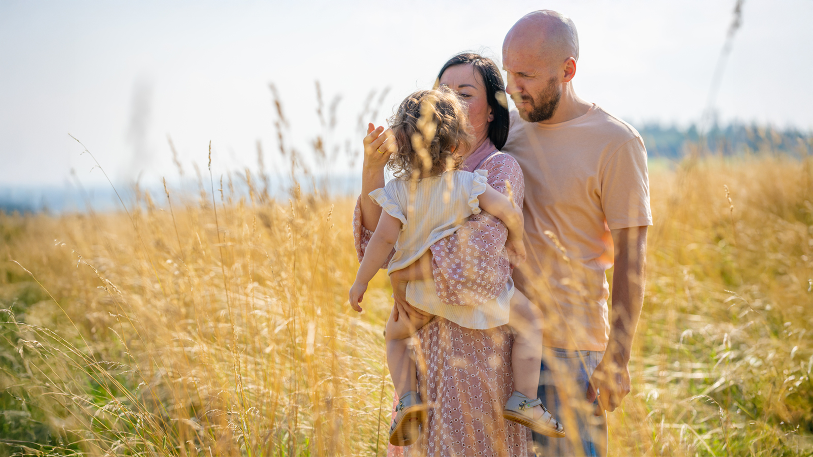 Eine junge Familie spaziert liebevoll durch ein goldenes Feld bei Magdeburg – Symbol für achtsame Eltern-Kind-Bindung, Geborgenheit und bindungsorientierte Familienbegleitung von Cozyfamily.