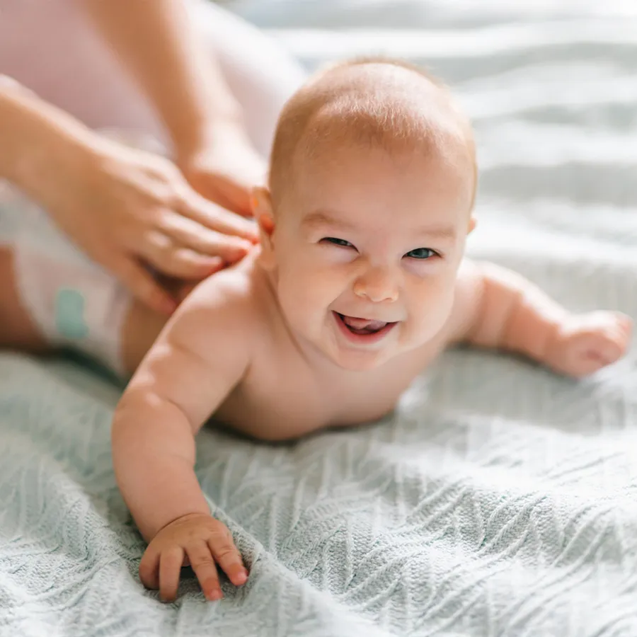 Ein lachendes Baby liegt auf einer weichen Decke und genießt eine sanfte Massage von der Mutter – Symbol für Geborgenheit, Entspannung und liebevolle Babywellness mit Babyyoga bei Cozyfamily in Magdeburg.