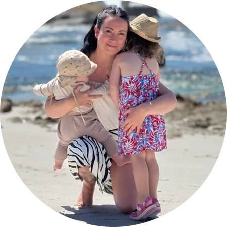Jessi von Cozyfamily kniet am Strand und hält ihre zwei kleinen Kinder im Arm – ein liebevoller Moment, der ihre zweite Mutterschaft und den Beginn ihres beruflichen Neuanfangs widerspiegelt.