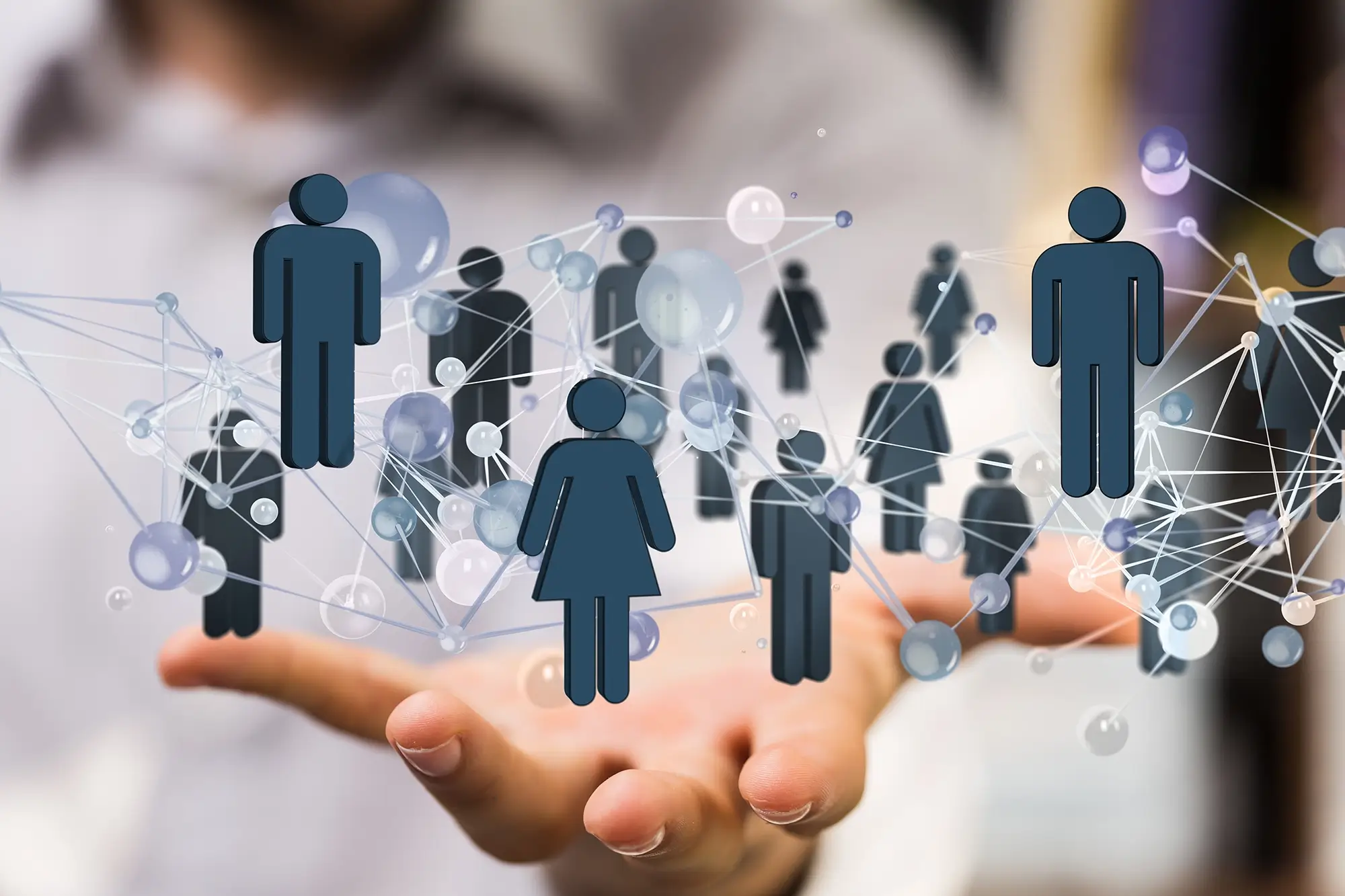 Eine geöffnete Hand, über der eine digitale Grafik schwebt, die durch Linien und Punkte vernetzte Personen-Icons darstellt – Symbol für Networking und soziale Strukturen.