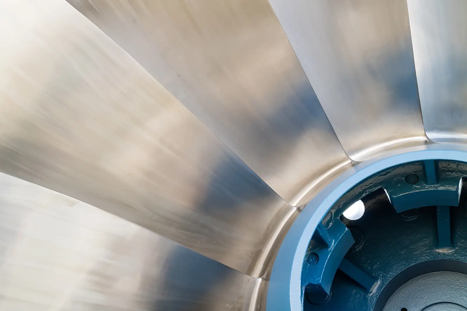 Nahaufnahme der glänzenden, metallischen Schaufeln eines industriellen Laufrads oder einer Turbine mit einem blau lackierten Gehäuseteil im Vordergrund.