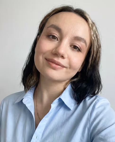 Smiling woman with half black and half blonde hair wearing a light blue collared shirt in front of a plain white background.
