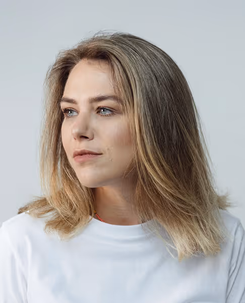 Portrait of a young woman with shoulder-length blonde hair looking to the side wearing a white shirt.