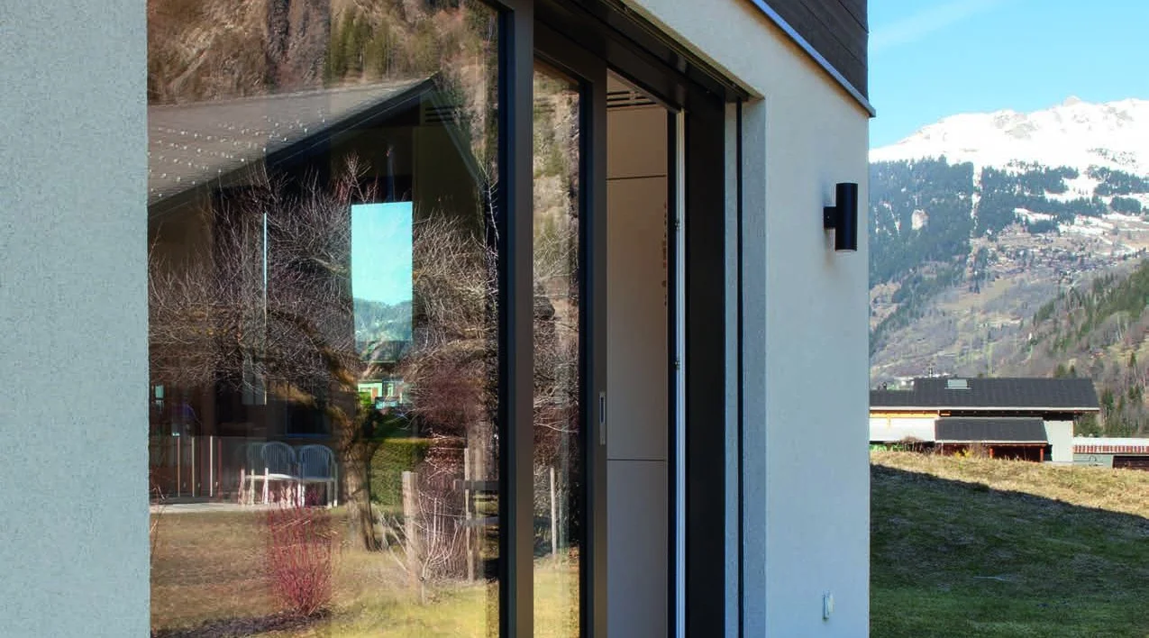 Große Schiebefensterfront mit schwarzem Rahmen an einem modernen Haus, im Hintergrund die verschneiten Schweizer Berge