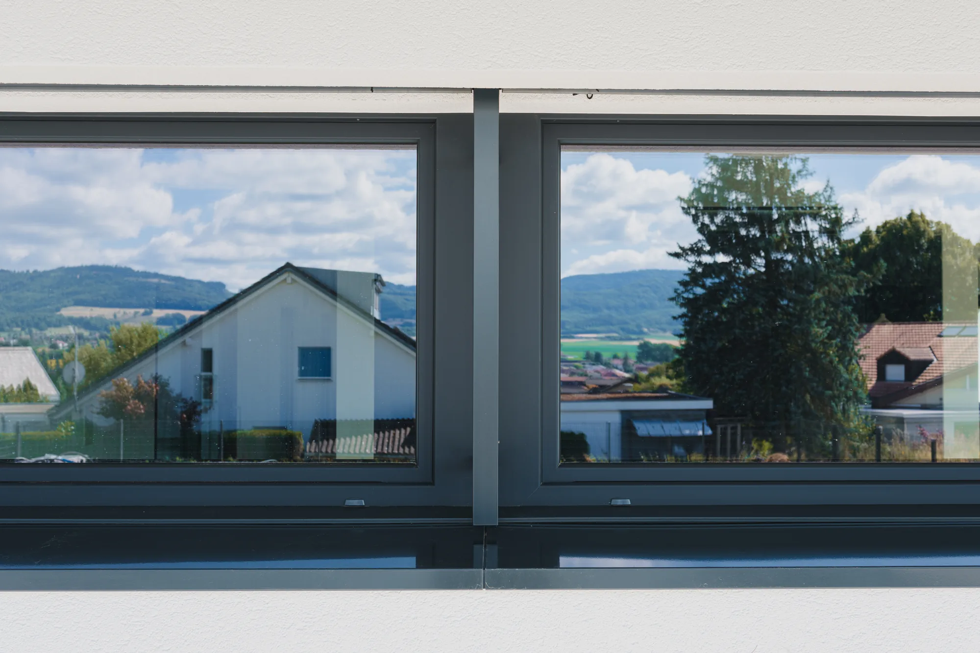 Fenêtre anthracite à deux vantaux vue de l'intérieur, donnant sur un village et les collines