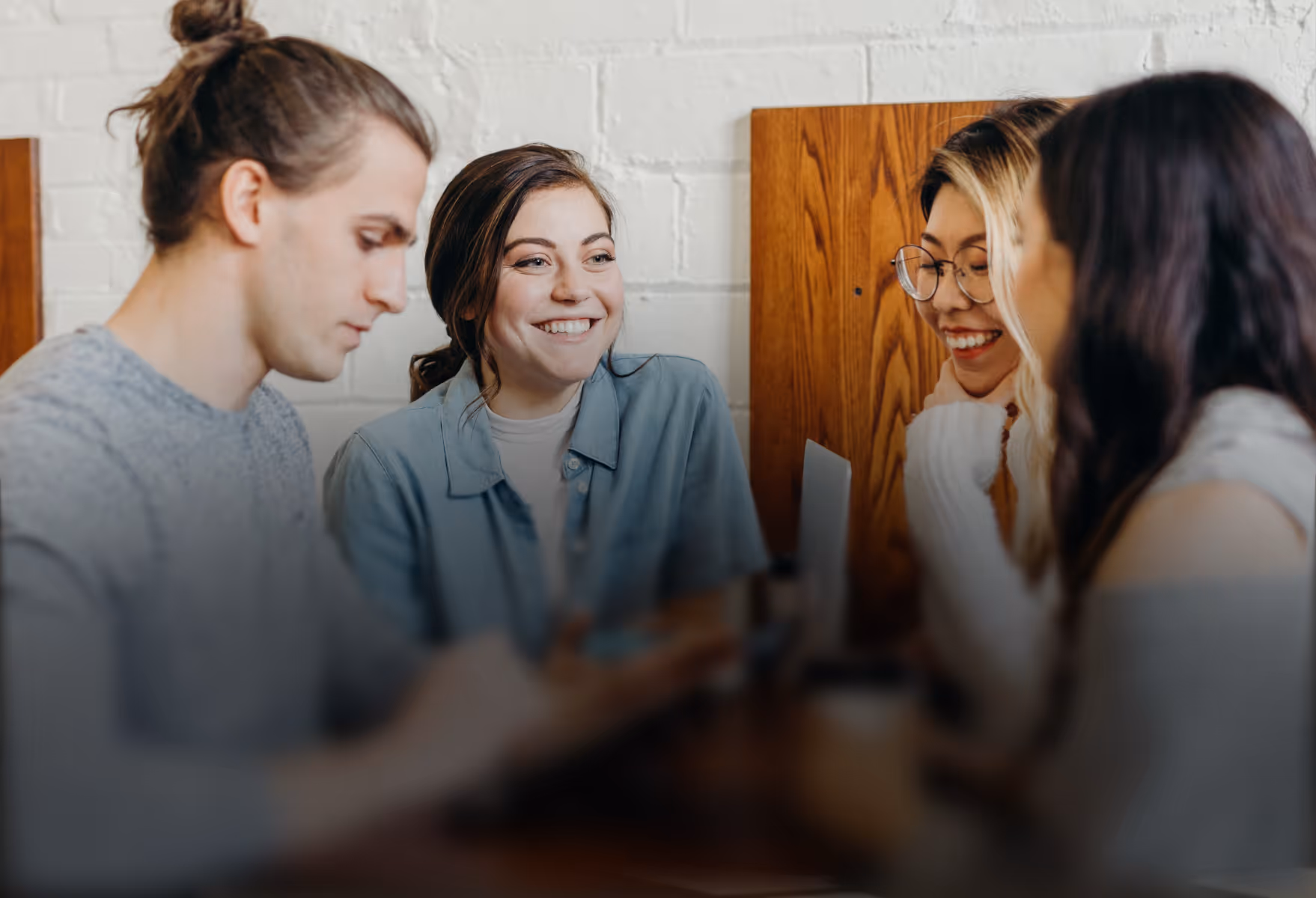 Vier junge Erwachsene sitzen zusammen, zwei Frauen lächeln und unterhalten sich an einem Tisch.