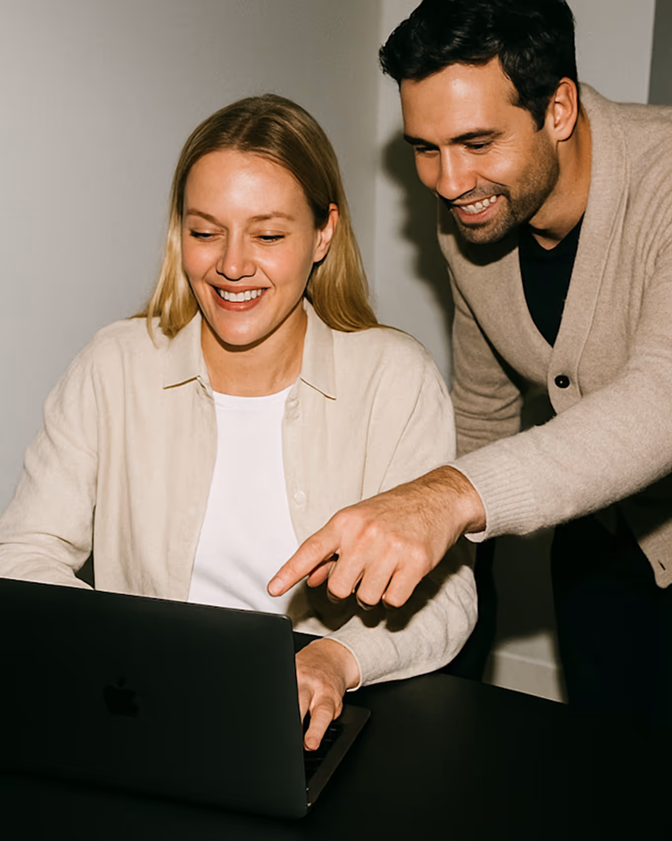 Ein lächelnder Mann zeigt auf einen Laptop-Bildschirm, während eine Frau daneben sitzt und ebenfalls lächelt.