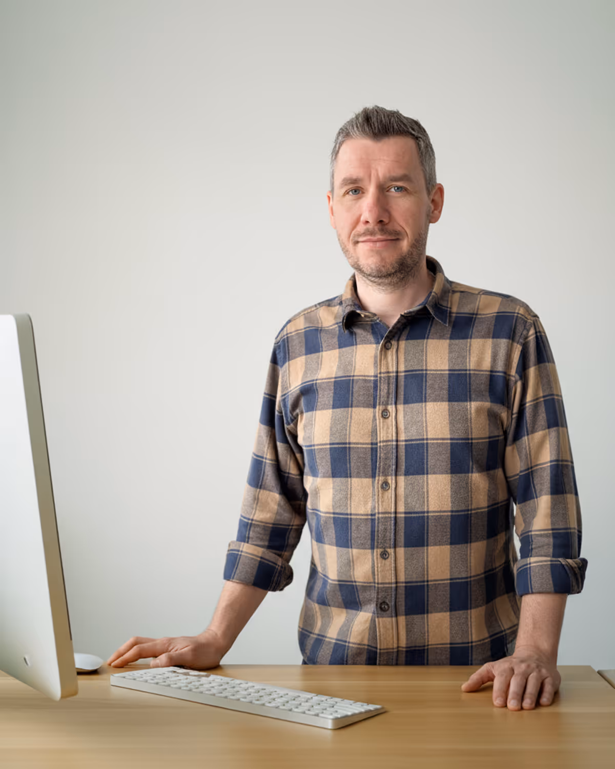 Dominik Albers, Geschäftsführer von meinMPP, steht mit kariertem Hemd an einem Schreibtisch neben einem Computer mit Tastatur.