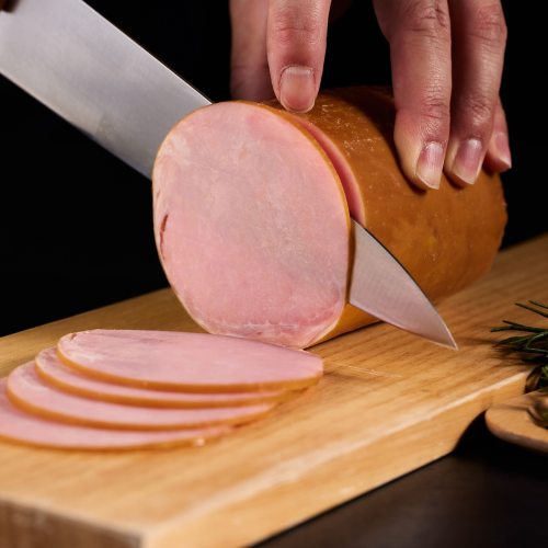 Apprenti charcutier coupant un jambon durant une formation métiers de bouche