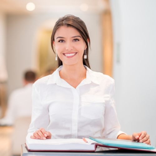Hôtesse d'accueil en chemise blanche assise devant des dossiers ouverts dans un environnement de bureau flou.