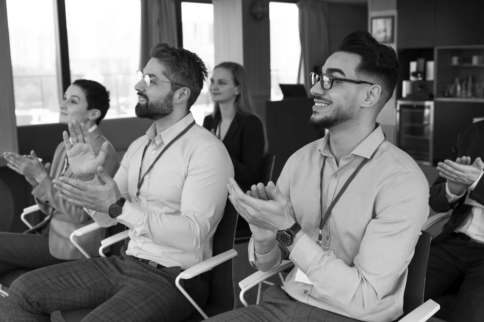 Group of diverse professionals sitting in chairs clapping and smiling during a meeting.