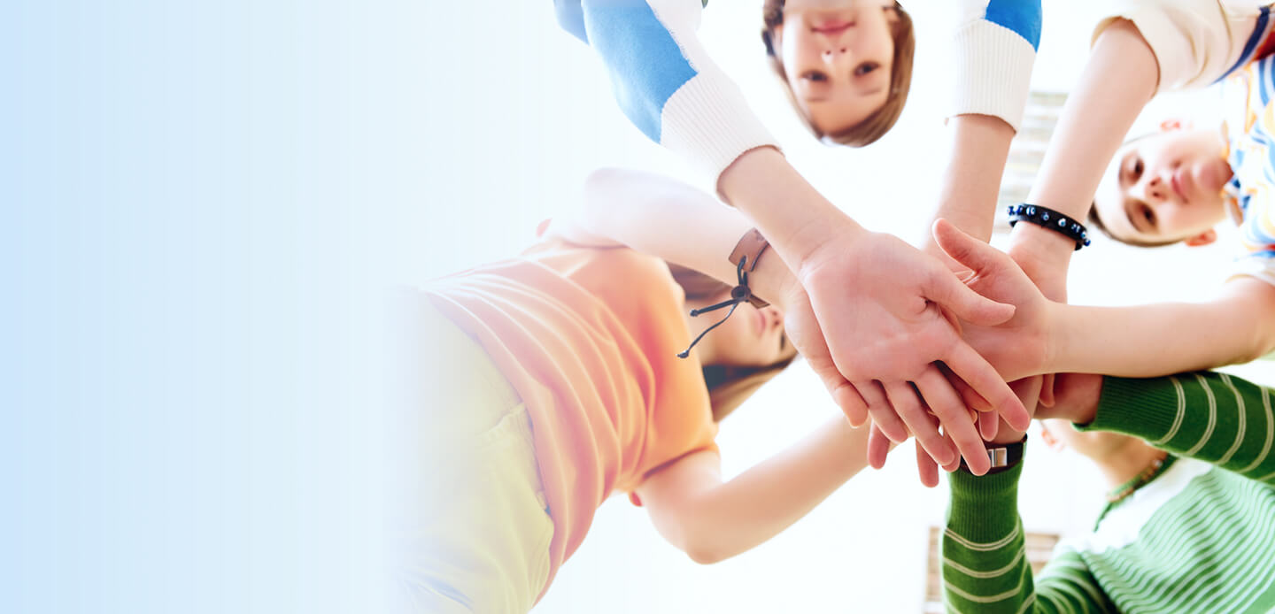 Group of children standing in a circle with hands stacked together, showing teamwork and unity.