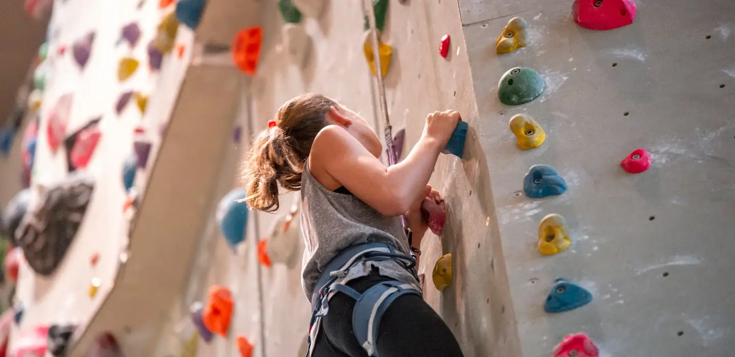 Young person climbing an indoor climbing wall using colourful handholds.