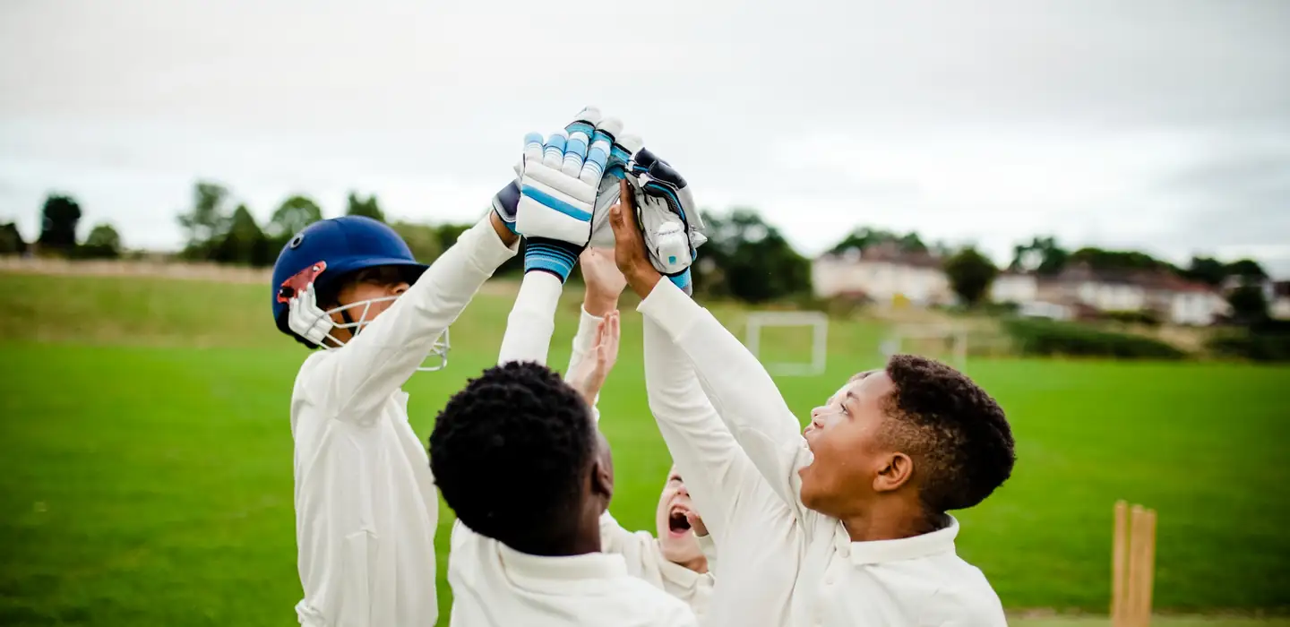 Children in cricket kit celebrating together on a grass playing field.